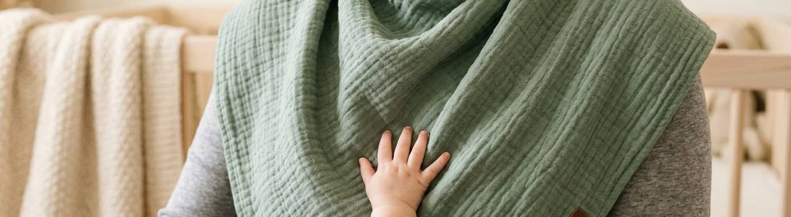 A parent wearing the sage Burp Bandana over their shoulders, their baby's hand resting on the fabric